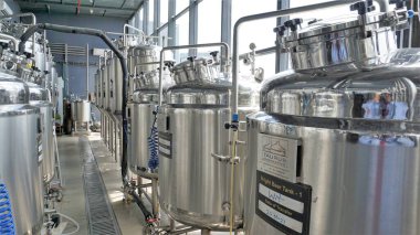Row of shiny metal micro brewery tanks or Fermentation mash vats in Brewery factory. Modern beer plant with brewering kettles, tubes and tanks made of stainless steel