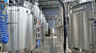 Row of shiny metal micro brewery tanks or Fermentation mash vats in Brewery factory. Modern beer plant with brewering kettles, tubes and tanks made of stainless steel