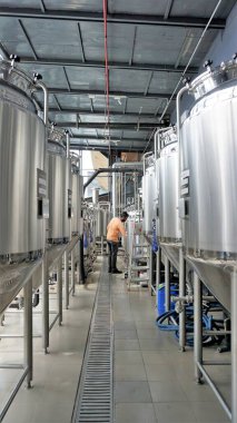 Row of shiny metal micro brewery tanks or Fermentation mash vats in Brewery factory. Modern beer plant with brewering kettles, tubes and tanks made of stainless steel