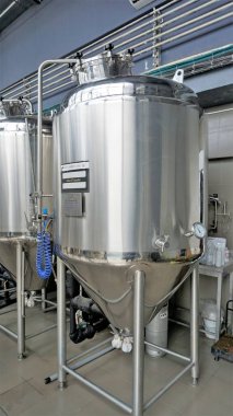 Row of shiny metal micro brewery tanks or Fermentation mash vats in Brewery factory. Modern beer plant with brewering kettles, tubes and tanks made of stainless steel