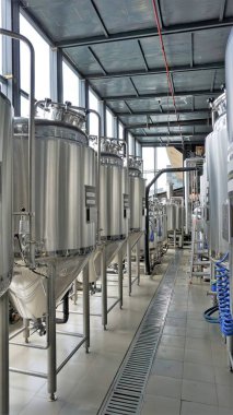 Row of shiny metal micro brewery tanks or Fermentation mash vats in Brewery factory. Modern beer plant with brewering kettles, tubes and tanks made of stainless steel