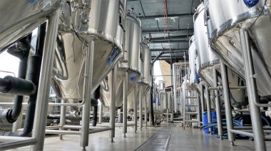 Row of shiny metal micro brewery tanks or Fermentation mash vats in Brewery factory. Modern beer plant with brewering kettles, tubes and tanks made of stainless steel