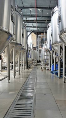Row of shiny metal micro brewery tanks or Fermentation mash vats in Brewery factory. Modern beer plant with brewering kettles, tubes and tanks made of stainless steel