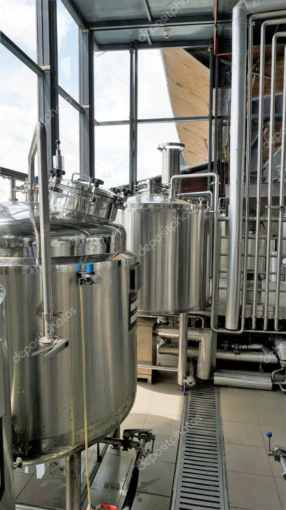 Row of shiny metal micro brewery tanks or Fermentation mash vats in Brewery factory. Modern beer plant with brewering kettles, tubes and tanks made of stainless steel