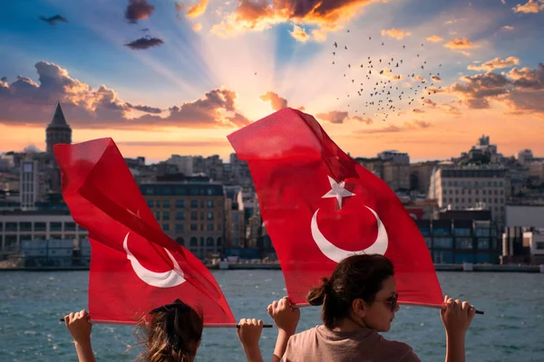 Istanbul, Turkey - July 2022: Little girls waving Turkish flag on a ship. Young girls waving Turkish flag at sunset. Turkish flag and a view of the Galata Tower in the background.