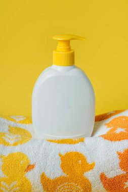 Sabun, şampuan şişesi ve sarı arka planda şirin ördekleri olan bebek havlusu. Banyo aksesuarları