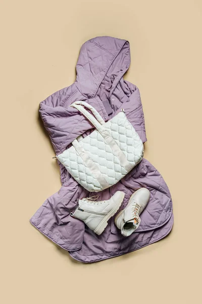 Violet oversize jacket with white quilted bag and boots on beige background. Fashion outfit, casual youth style, sports. Stylish autumn or spring  clothes.