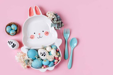 Paskalya sofrası dekorasyonu, paskalya yumurtası ve pembe arka planda şekerlemeli tavşan şeklinde şirin bir tabakla. Mutlu Paskalyalar. Paskalya yemeği için fikir