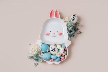 Paskalya yumurtası, şeker ve bej arka planda çiçekli tavşan şeklinde şirin bir tabak. Mutlu Paskalyalar. 