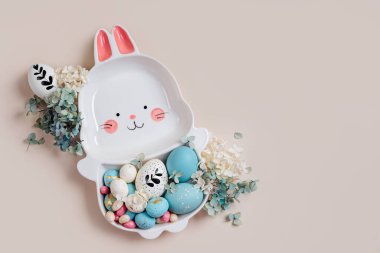 Paskalya yumurtası, şeker ve bej arka planda çiçekli tavşan şeklinde şirin bir tabak. Mutlu Paskalyalar. 