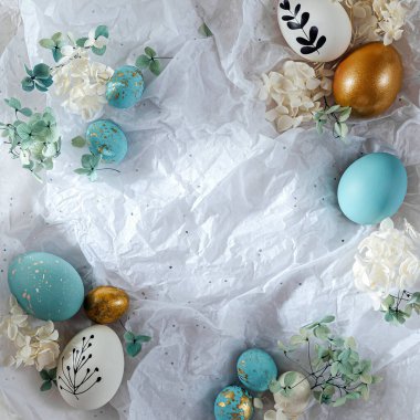 Şekerli Paskalya yumurtaları ve beyaz kağıtta fotokopi alanı olan çiçekler. Mutlu Paskalyalar. Paket kağıdında beyaz, mavi ve altın yumurta