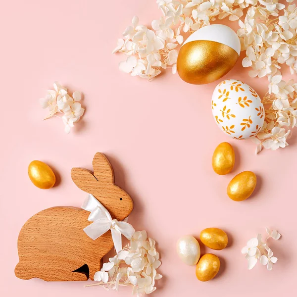 Osterhase Und Goldene Eier Mit Süßigkeiten Und Blumen Auf Pastellrosa lizenzfreie Stockfotos