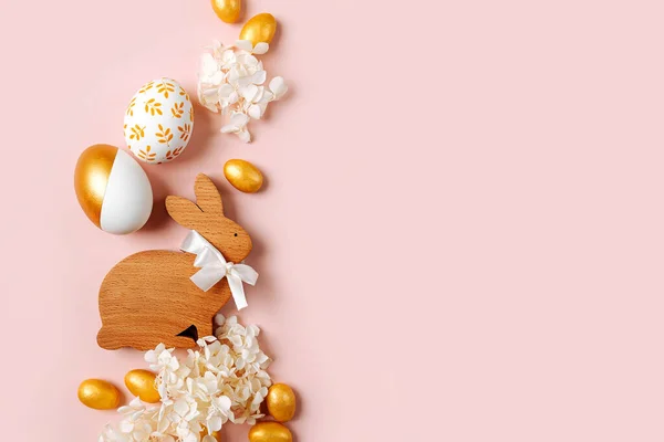 Osterhase Und Goldene Eier Mit Süßigkeiten Und Blumen Auf Pastellrosa lizenzfreie Stockbilder