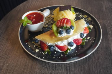 Yakın plan çıtır kraker ve meyveli dondurma tutku meyvesi, taze çilekli meyve ve beyaz seramik kapta, ahşap masa arkasında çilekli reçel.                          