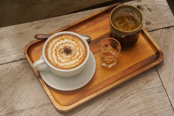 hot coffee in a white ceramic cup and honey in a glass and water in a ceramic glass, place on a rectangular wooden tray,  on the wooden table background, food and drinks, copy space