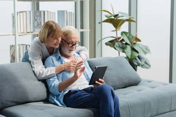 Yaşlı, üst sınıf aile çifti, günlük kıyafetlerini giyer ve akıllı tablet kullanır, gülümser, mutlu ve romantik bir şekilde oturma odasında gülümserler..