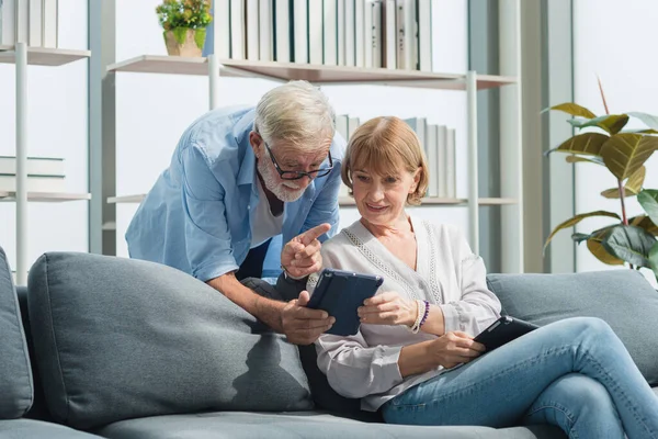 Yaşlı, üst sınıf aile çifti, günlük kıyafetlerini giyer ve akıllı tablet kullanır, gülümser, mutlu ve romantik bir şekilde oturma odasında gülümserler..