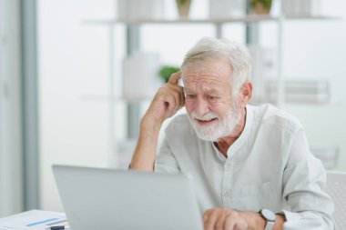 Beyaz giysili kıdemli yaşlı adam evde oturuyor ve modern bir çalışma odasında çalışırken kafası karışıyor..