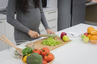 Gri kazaklı hamile kadın modern mutfak odasında yemeğini hazırlıyor..