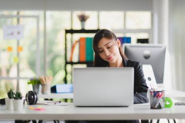 Business Asian woman in formal suit working and typing in her laptop with smiling in modern interior office workplace 
