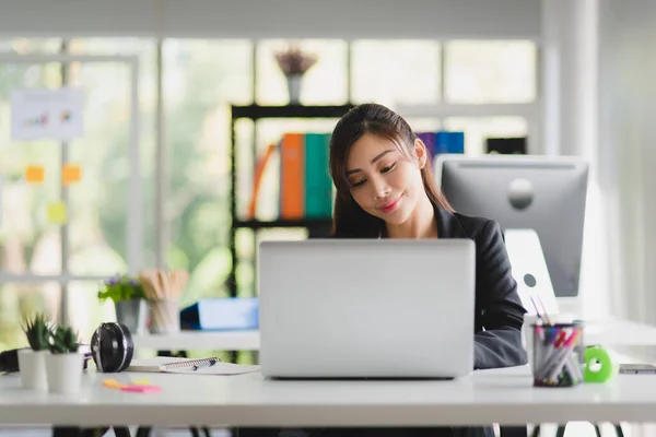 Business Asian woman in formal suit working and typing in her laptop with smiling in modern interior office workplace 
