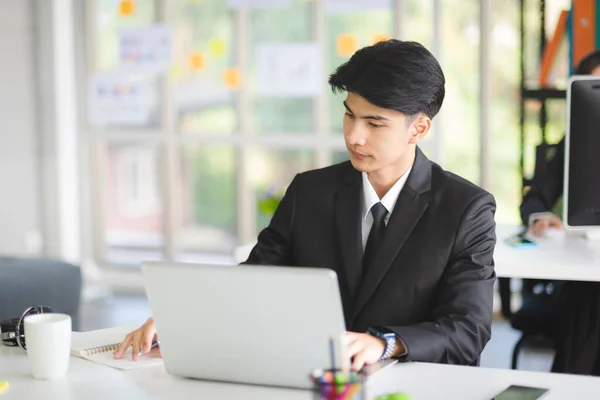 Business Asian man in formal manager looking suit working with smiling and happy emotion in modern interior office workplace.