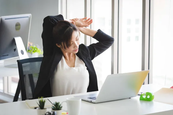 Business Asian woman in formal suit working and stretch her body to relax herself from stress in modern office workplace room.