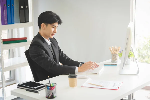 Business Asian man in formal manager looking suit working with smiling and happy emotion in modern interior office workplace.