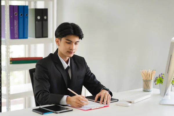 Business Asian man in formal manager looking suit working and typing on keyboard with smiling and happy in modern interior office workplace.
