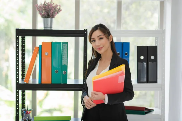 Portrait of business Asian woman in formal suit holding documents in modern office workspace room.