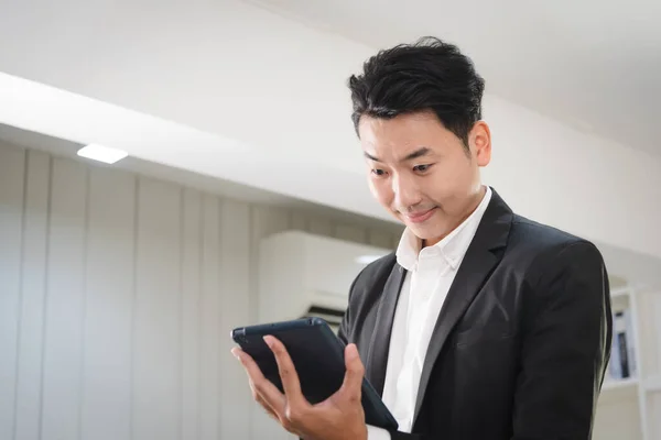 Young business Asian man in formal outfit using tablet for working with confident and focus in modern workplace.