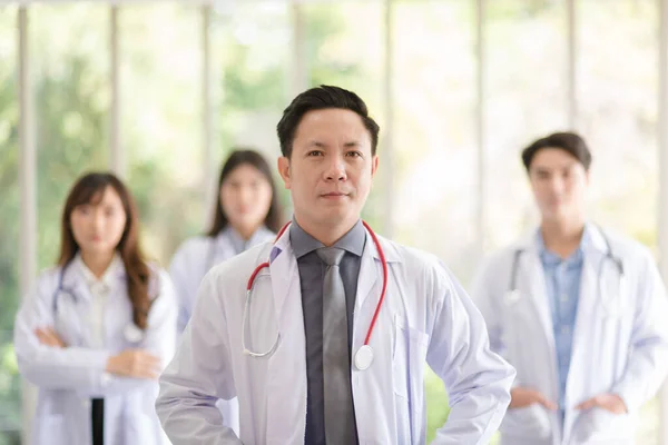 Group of Asian doctors team portrait in white lab coat professional uniform standing with colleagues in background.