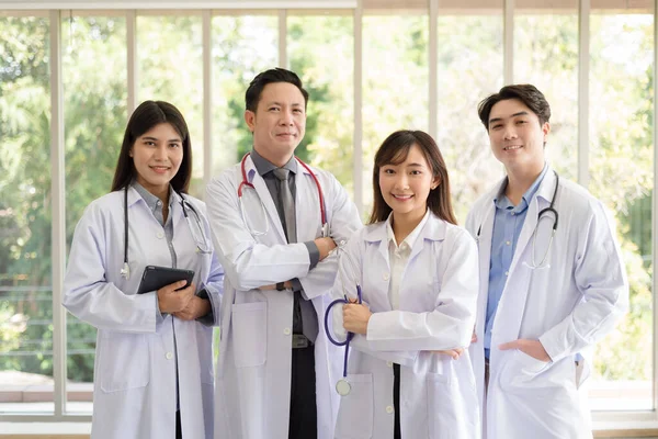 Group of Asian doctors team portrait in white lab coat professional uniform standing with colleagues in background.
