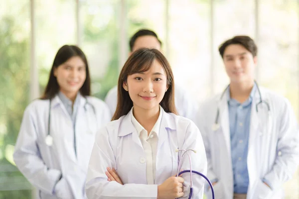 Group of Asian doctors team portrait in white lab coat professional uniform standing with colleagues in background.
