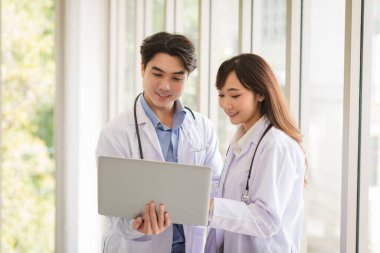 Group of Asian doctors team portrait in white lab coat professional uniform standing and using laptop with other colleagues in background.