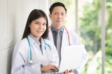Group of Asian doctors team portrait in white lab coat professional uniform standing with colleagues in background.