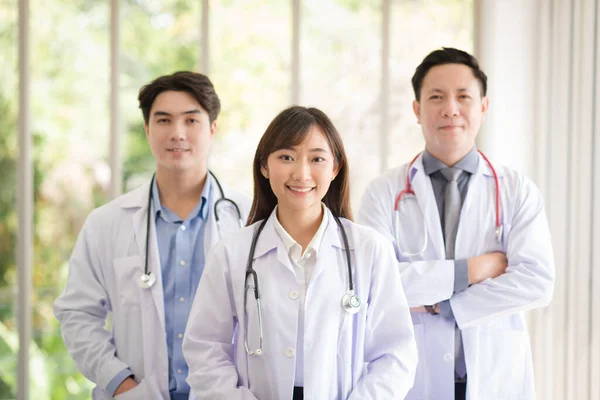 Group of Asian doctors team portrait in white lab coat professional uniform standing with colleagues in background.