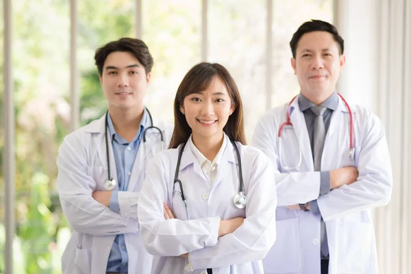 Group of Asian doctors team portrait in white lab coat professional uniform standing with colleagues in background.
