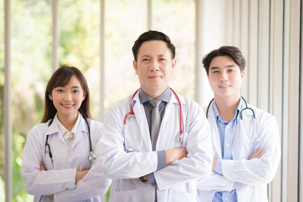 Group of Asian doctors team portrait in white lab coat professional uniform standing with colleagues in background.