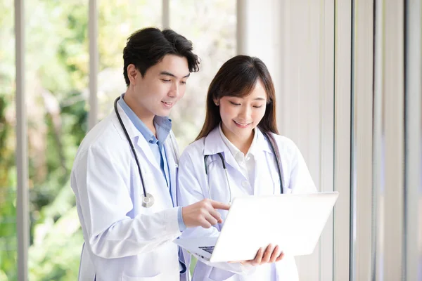 Group of Asian doctors team portrait in white lab coat professional uniform standing and using laptop with other colleagues in background.