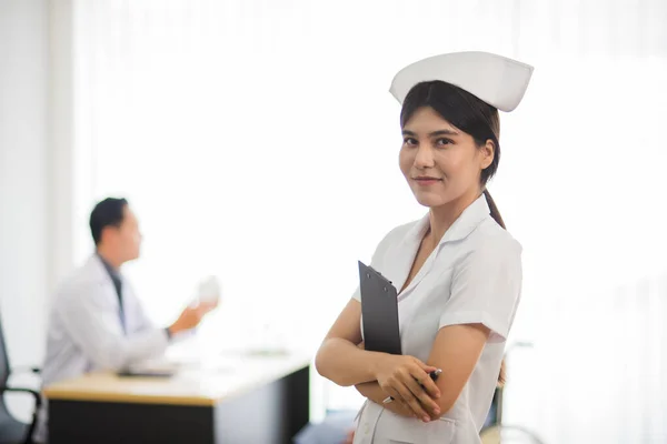 Asian nurse woman in professional working uniform standing with smile and happiness with patient and doctor in background.