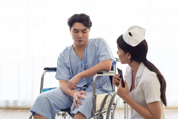 Asian nurse in working uniform taking care of patient sitting on wheel chair.