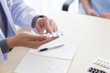 Profesyonel iş üniformalı Asyalı doktor hastasına ilaç ve ilaç semptomlarını tartışır ve açıklar..