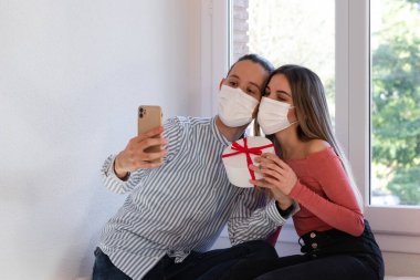 Kadın ve erkek yüz maskesi takmış bir şekilde ailelerine video görüşmesi yapıyorlar.