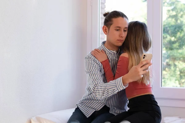 Άντρας αγκαλιάζει γυναίκα ενώ κοιτάζει smartphone — Φωτογραφία Αρχείου