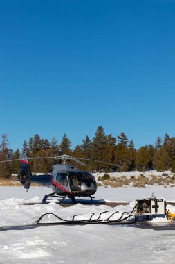 Helikopter helikopter pistinde yakıt ikmali yapıyor. Ağaçlar ve karla çevrili.
