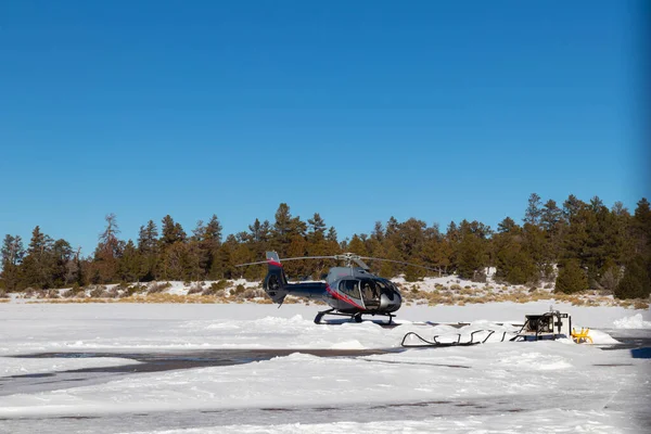 Helikopter kış günü helikopter pistinden havalanıyor. Etrafı ağaçlar ve karlarla çevrili.