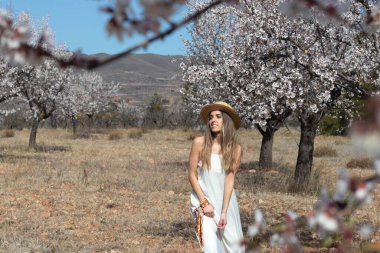 Genç, mutlu sarışın kadın beyaz bir yaz elbisesi ve hasır şapka giyiyor.