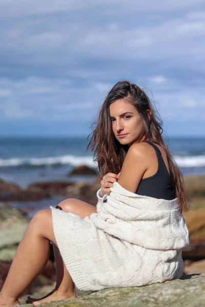 Brunette woman sitting looking at the camera in a knitted jacket on the beach — Stock Photo, Image