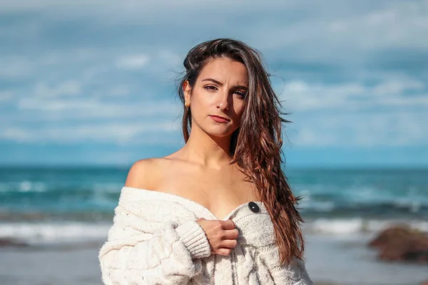 Beautiful and brunette woman looking to the camera on the beach in a sweater — Stock Photo, Image